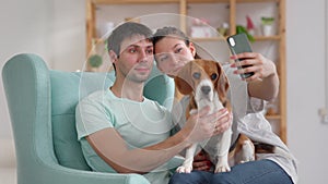 Young couple with dog taking selfie photo and sitting on sofa in home room spbi.