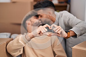 Young couple doing heart symbol with hands sitting on sofa at new home