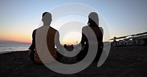 Young couple doing morning meditation on beach at sunrise