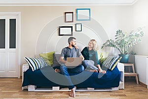 Young couple doing shoppings online on the sofa at home with laptop, looking at each other and smiling