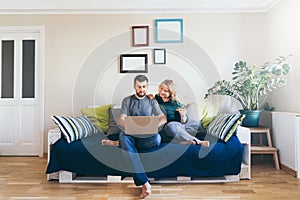 Young couple doing shoppings online on the sofa at home, looking at laptop screen and smiling photo