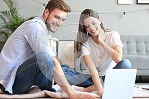 Young couple doing some online shopping at home, using a laptop on floor