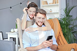 Young couple doing some online shopping at home, using smart phone on the sofa