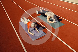 Young couple doing sports in the stadium lying on yoga mats