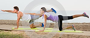 Young couple doing yoga poses together on sea beach