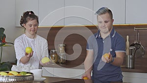 Young couple with Down Syndrome juggle at kitchen