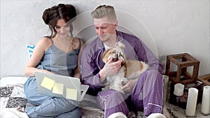 Young couple dressed in pajamas sitting on bed together.