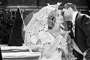 Young couple dressed in vintage costume relaxing with man on one knee, kissing on lawn in front of stately home