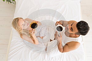 Young Couple Drink Coffee Sitting In Bed, Happy Smile Hispanic Man And Woman Top Angle View