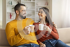 Young couple drinking coffee together, sitting on couch in living room