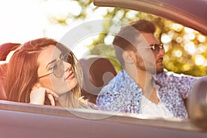 Young Couple Driving Along Country Road In Open Top Car