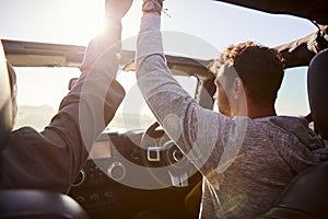 Young couple driving with sunroof open and hands in the air