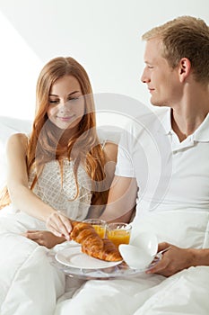 Young couple eating breakfast in bed