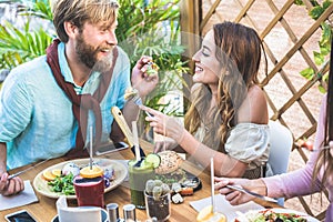Young couple eating brunch and drinking smoothie bowl at vintage bar - Happy people having a healthy lunch and chatting in trendy