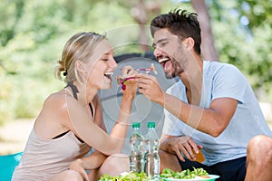 Young couple eating from eachothers forks while camping