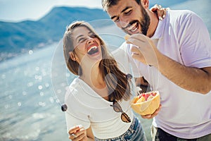 Couple eating fruit on the beach- summer party with friends and healthy food concept