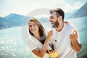 Couple eating fruit on the beach- summer party with friends and healthy food concept