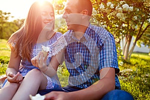 Young couple eating ice-cream and chatting outside. Woman and man chilling out in spring garden at sunset. Lifestyle