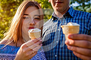 Young couple eating ice-cream and chatting outside. Woman and man chilling out in spring garden at sunset. Lifestyle