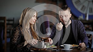 A young couple eating a salad in a restaurant, a man and a pretty woman talking during a meal, on the table are cups of