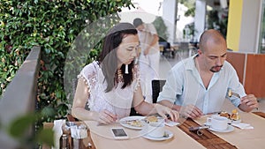 Young couple eating and talking during breakfast by table in the outdoor cafe