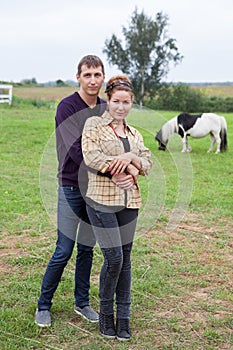 Young couple embracing in farmland, portrait of young man nand woman in countryside, horse is on background