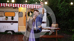 Young couple embracing standing in front trailer they living in with sparklers celebrating, dancing and smiling. Happy