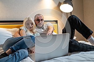 Young couple is engrossed in content on laptop, man and woman entertainment or collaboration, while relaxing in bed