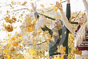 Young couple enjoying falling autumn leaves in park