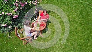 Young couple enjoying food and drinks in beautiful roses garden on romantic date, aerial top view from above of man and woman