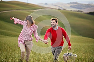 A young couple is enjoying nature while walking a large meadow by holding hands. Relationship, love, together, picnic, nature