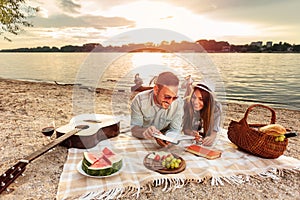 Young couple enjoying a picnic at the beach. Lying on the picnic blanket, reading books