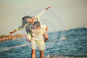 Couple enjoying summer holidays. Handsome young man giving piggyback ride to girlfriend on beach