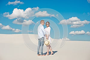 Young couple enjoying the sunset in the dunes. Romantic traveler walks in the desert. Adventure travel lifestyle concept