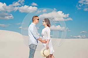 Young couple enjoying the sunset in the dunes. Romantic traveler walks in the desert. Adventure travel lifestyle concept