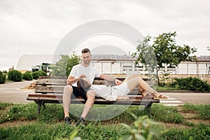 Young couple enjoying time together - woman lying on knees of man on bench on summer sunny day. Smiling man and woman