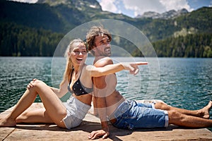 A young couple enjoying the view and sunbathing on the dock at the lake during mountain hiking. Trip, nature, hiking
