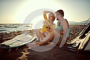 Young couple enoying in sunset at the beach, sitting together at the beach with legs intertwined, cuddling. copy space