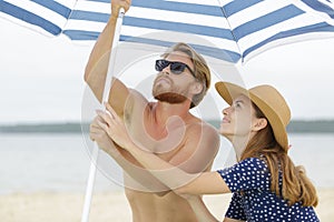 young couple erecting parasol on beach