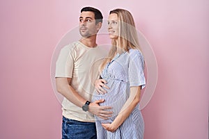 Young couple expecting a baby standing over pink background looking to side, relax profile pose with natural face and confident