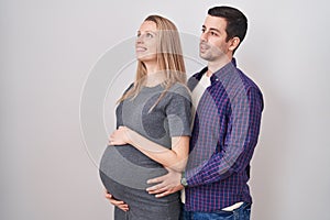 Young couple expecting a baby standing over white background looking to side, relax profile pose with natural face and confident