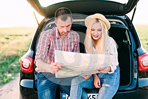 Young couple exploring a map sitting in the trunk of a car with things to travel