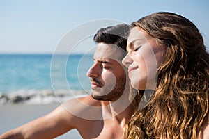 Young couple with eyes closed sitting together at beach