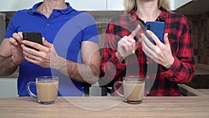 Young couple, family, man and woman with smartphones at home in the kitchen. Internet addiction concept