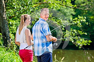 Young couple fishing or angling standing on river shore photo