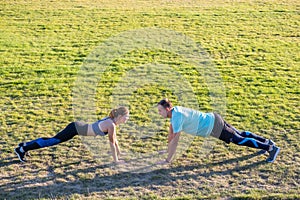 Young couple of fit sportsmen boy and girl doing exercise on green grass of public stadium outdoors