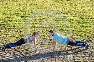 Young couple of fit sportsmen boy and girl doing exercise on green grass of public stadium outdoors
