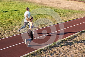 Young couple of fit sportsmen boy and girl running while doing exercise on red tracks of public stadium outdoors