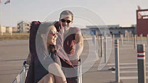 Young couple of friends having fun in the parking lot with a supermarket trolley.Slow motion.