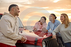 Young Couple With Friends Standing Chatting By Car At Beach Watching Sunrise Together photo